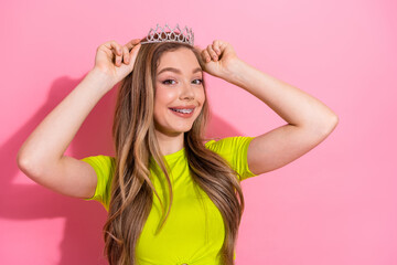 Beautiful young girl posing with a crown on her head, cheerful and stylish, against a pink background © deagreez