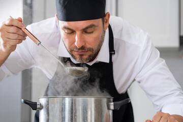 modern chef in professional uniform. close-up on the hand of male chef who is stirring soup in pot...