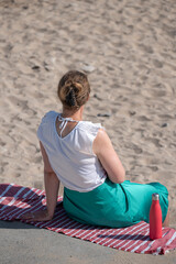 Saint-Aubin-Sur-Mer, France - 08 11 2025: A young blonde woman sitting on the pier feet on the sand...