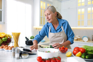 Senior woman using tablet while cooking at white marble table in kitchen