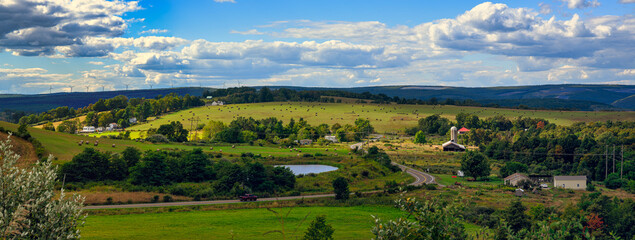 Preston County, West Virginia, USA   Rolling farmland dotted with hay bales stretches toward the horizon, where wind turbines trace the ridgeline beneath a sky layered with late-summer clouds. © Igor Os