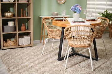 Stylish setting with plates and vase of flowers on wooden table in dining room. Interior design