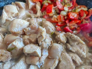 Fried chicken breast with sliced red peppers cooking in pan.