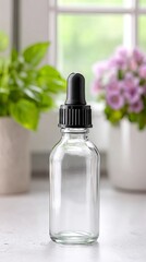 Clear glass dropper bottle with black lid stands on a countertop surrounded by green plants and purple flowers, showcasing a minimalist and elegant design for product presentation