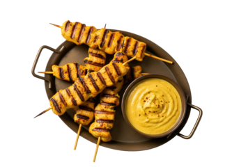 Grilled chicken skewers with a rich, golden-yellow sauce are artfully arranged on a dark metal platter, creating a visually appealing food presentation.