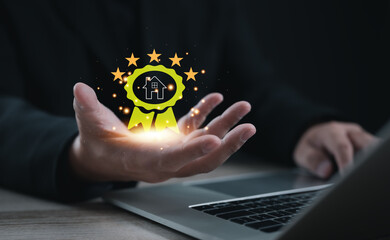 Hand holding digital award badge with house icon and five stars. Concept of real estate excellence, property recognition, quality assurance, best service, and high-value housing achievement.