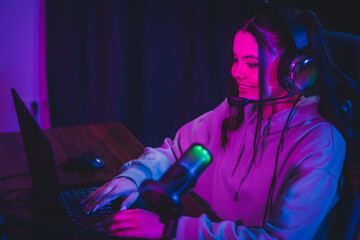 Addicted gamer woman gamer with headset and microphone live streaming at home using laptop in neon...