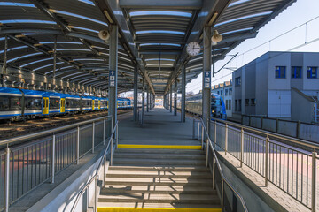 Obraz premium Train station platform with stairs leading to waiting trains under an open canopy, providing shelter and access for rail passengers.