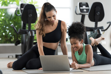 Fototapeta premium African American young girl and coach or personal trainer using laptop computer for training media online in fitness gym