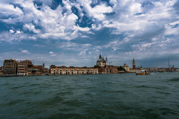 Venice cityscape on a wavy day with a boat floating over the waters and a cloudy sky above the...