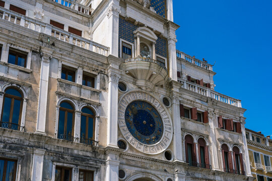 Detailed view of an ornate astronomical clock tower with blue accents against a clear sky on a historic building in Europe. - Powered by Adobe