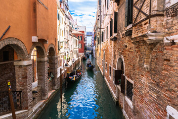 Venetian Canal View: Gondolas navigate narrow waterways framed by historic buildings under a partly cloudy sky. Beautiful, old architecture.