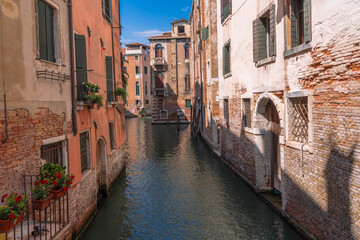 Venetian canal: old brick buildings flank the serene waterway, creating a picturesque scene under the clear blue sky. Timeless European charm.