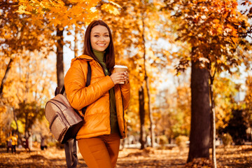 Beautiful young woman enjoying an autumn day in a charming park with vibrant foliage holding a...