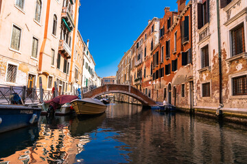 Venice canal: Boats glide under a bridge, framed by historic buildings under a blue sky. Timeless beauty.