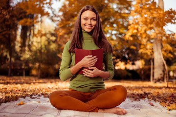 Charming young woman enjoying leisure with a book in vibrant fall park scenery, surrounded by autumn foliage and natural beauty