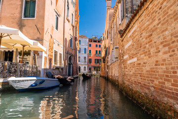 Venetian canal scene with boats, colorful buildings, and blue skies, evoking a sense of history, charm, and beauty.