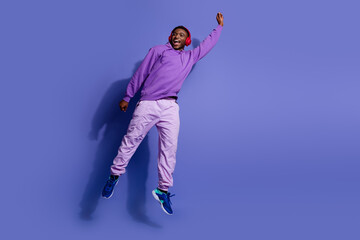 Young man in purple attire energetically posing with headphones, trendy casual fashion on violet...