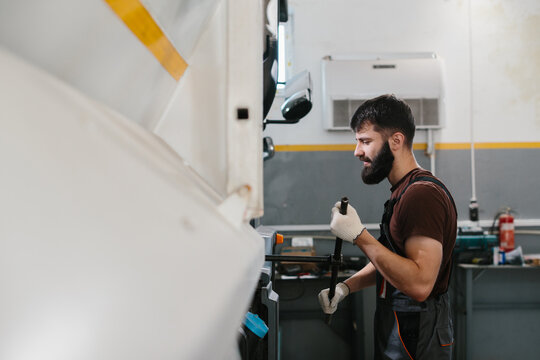 Mechanic repairing truck wheel in garage: caucasian man using wrench
