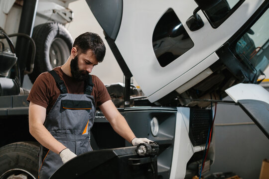 Mechanic repairing truck engine in garage using tools and flashlight - Powered by Adobe