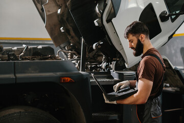 Mechanic diagnosing truck engine with laptop in repair shop