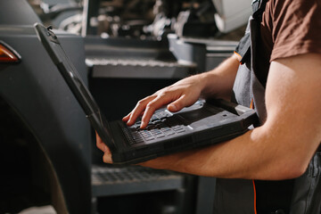 Auto mechanic using laptop while repairing truck in garage