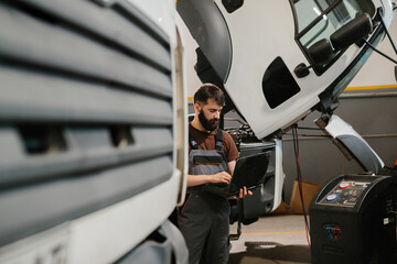 Mechanic using laptop diagnosing truck malfunction in garage