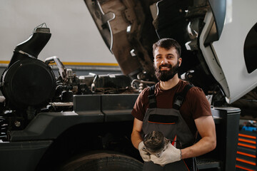 Smiling mechanic holding truck part after fixing engine in garage