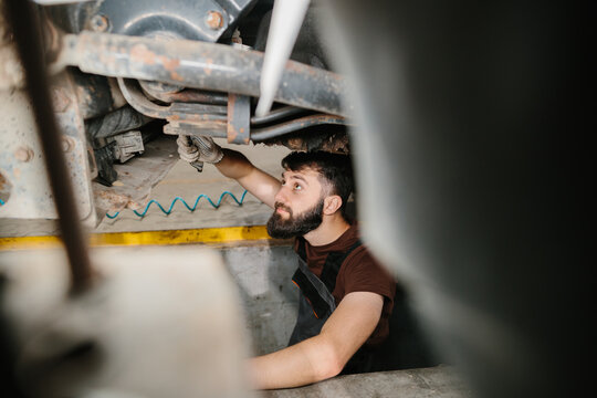 Auto mechanic repairing truck in garage: caucasian male fixing vehicle