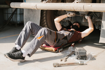 Mechanic repairing truck using wrench lying on creeper