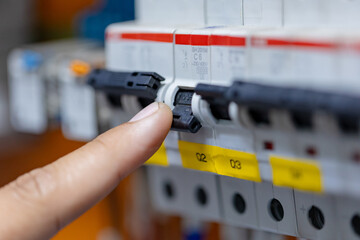 A person's finger pushes a white circuit breaker switch in a row of multiple breakers on an electrical panel.