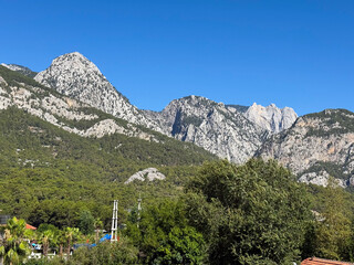 Mountain landscape with rocky peaks, forest slopes and blue summer sky. Nature, wilderness,...