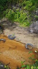 Polluted stream with car tires and garbage in muddy water surrounded by green plants