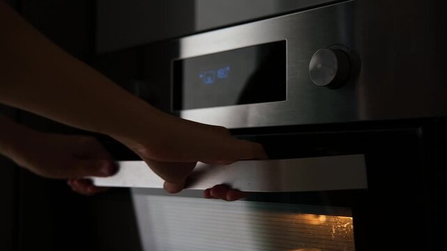 Side view of the woman turning on the electrical oven in the kitchen to baking dessert. Checking readiness of the food