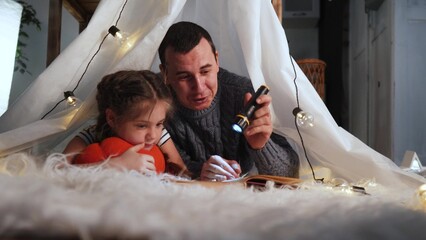 happy family at home dream. dad and daughter happy family lockdown at home reading a book in the evening homemade wigwam house. kid dream coronavirus concept. dad daughter read stay home book