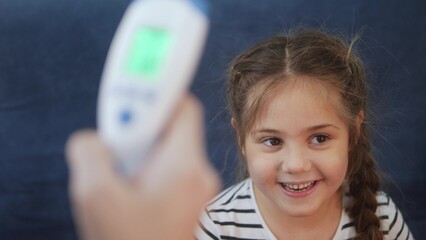 mom measures the temperature with an infrared thermometer, the little girl fell ill coronavirus. stay home lockdown social distance coronavirus covid 19. temperature measurement during coronavirus