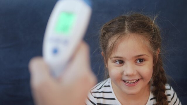 mom measures the temperature with an infrared thermometer, the little girl fell ill coronavirus. stay home lockdown social distance coronavirus covid 19. temperature measurement during coronavirus - Powered by Adobe