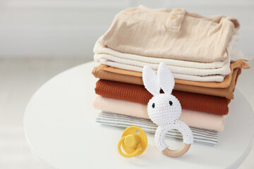 Stack of clean baby clothes and accessories on white table indoors, closeup. Space for text
