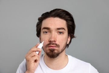 Young man with acne problem applying cream onto his face on light grey background
