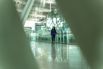 A young Caucasian woman with fair skin wearing a blue sweatshirt walks through the airport waiting for her boarding time. She carries a backpack and is dressed comfortably for traveling. Vigo, Spain