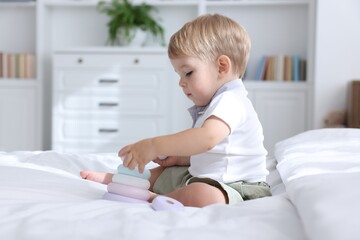Cute little baby playing with toy pyramid on bed at home