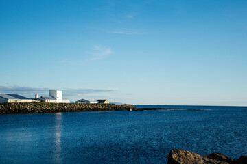 Coastal landscape with buildings and blue sea under clear Icelandic sky