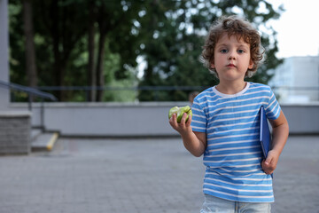 Cute little boy eating apple outdoors, space for text. School lunch