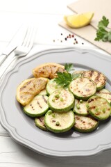 Delicious fried courgette slices with lemon and parsley served on white wooden table, closeup