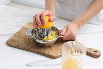Making juice. Woman with orange using juicer at white marble table indoors, closeup