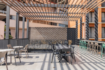 Modern outdoor terrace with tables and chairs under geometric shadows, contemporary architecture and stylish urban design.