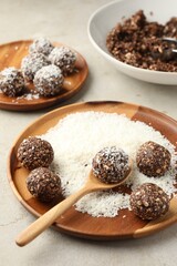 Making tasty chocolate candies with nuts and coconut flakes at light table, closeup