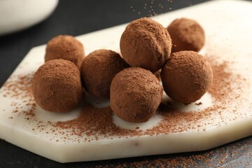 Tasty chocolate candies with cocoa powder on black table, closeup