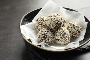 Tasty chocolate candies with nuts and sesame seeds in bowl on grey table, closeup