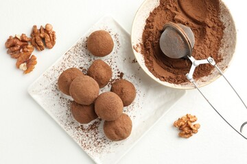 Tasty chocolate candies with cocoa powder and walnuts on white table, flat lay